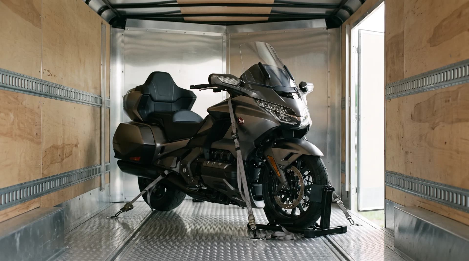 Touring motorcycle chocked upright and strapped inside a wood-lined enclosed trailer