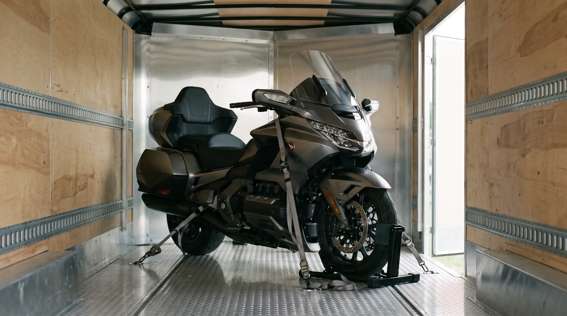 Touring motorcycle chocked upright and strapped inside a wood-lined enclosed trailer